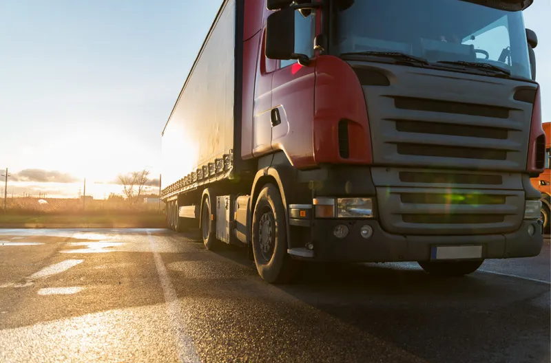 Rode vrachtwagen met oplegger geparkeerd op een terrein bij zonsondergang